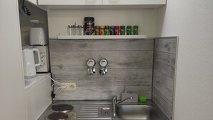 A compact kitchen with a built-in stove, a sink, and a microwave. There are spice jars on a shelf above the stove. - Apartment Classic (Jülich)