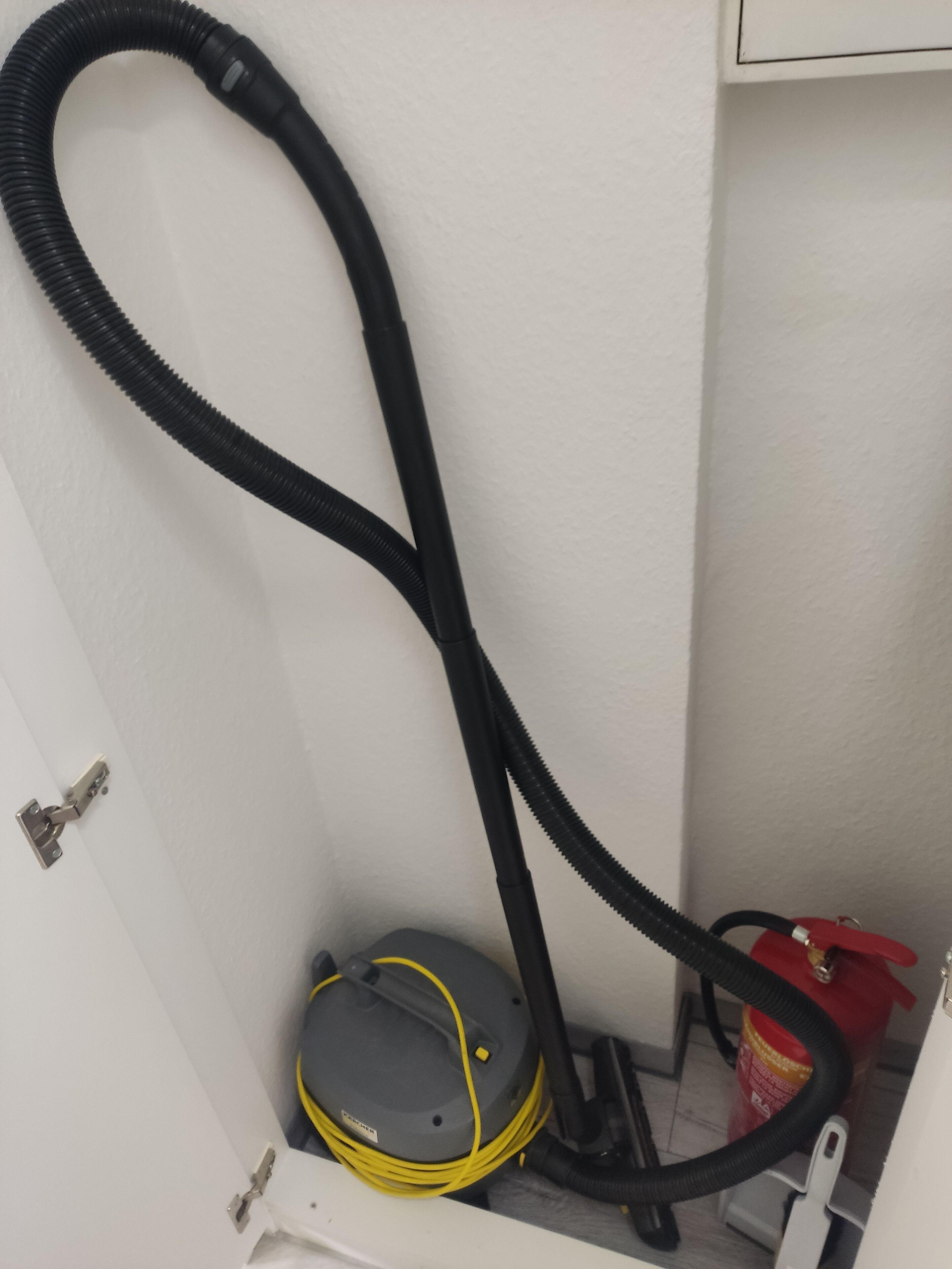 A vacuum cleaner with a hose and a canister in a corner.