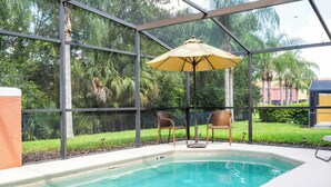A pool area with a glass enclosure, two wicker chairs, and a yellow umbrella. - Family-Friendly 3BR Townhome at Encantada Resort ● Pool, BBQ & Near Disney! (Kissimmee)
