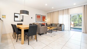 A modern living room with a dining area, a sofa set, and a large window with curtains. - Family-Friendly 3BR Townhome at Encantada Resort ● Pool, BBQ & Near Disney! (Kissimmee)