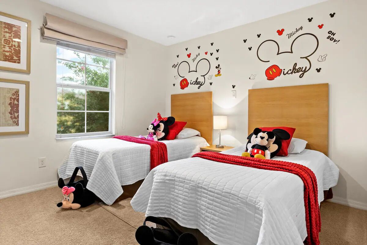 Une chambre d’hôtel avec deux lits, chacun doté d’une tête de lit sur le thème de Mickey Mouse, de draps blancs et d’éléments décoratifs rouges.