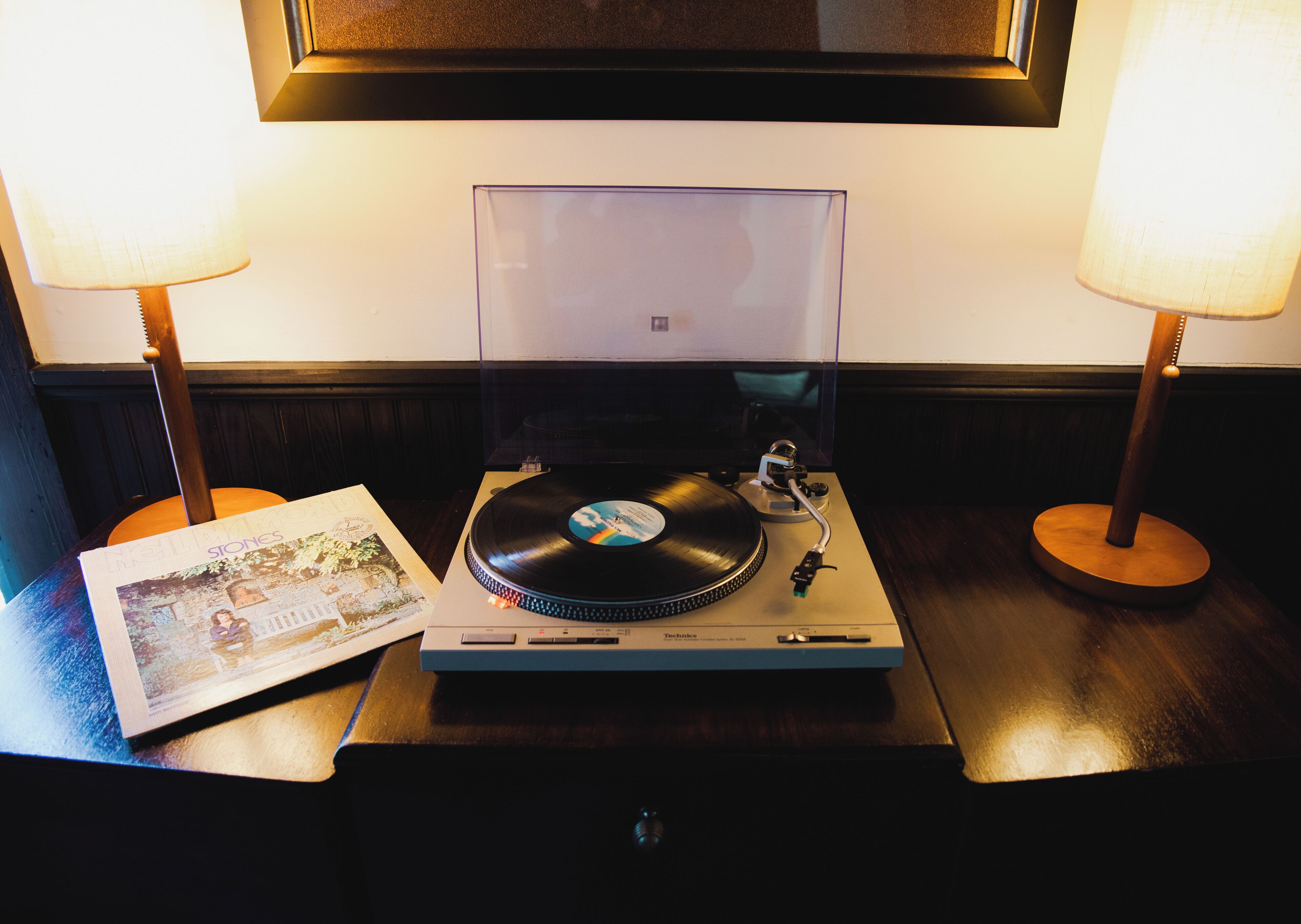 Un tocadiscos con un disco de vinilo, un cuadro enmarcado y dos lámparas sobre una mesa de madera.