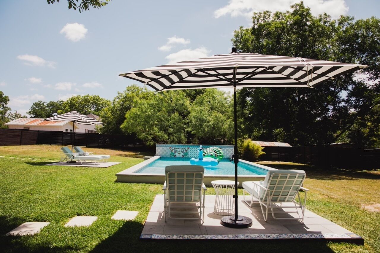 A backyard with a swimming pool, lounge chairs, and an umbrella.