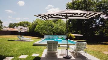 A backyard with a swimming pool, lounge chairs, and an umbrella.