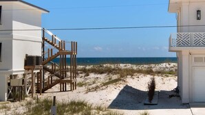 Une propriété située en bord de mer, avec un escalier en bois menant à un bâtiment blanc, une plage de sable et une vue dégagée sur l’océan.