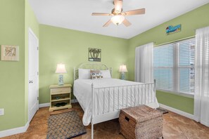 A bedroom with a bed, nightstands, a ceiling fan, a window with curtains, and a door. - Baywatch G5 (Pensacola Beach)