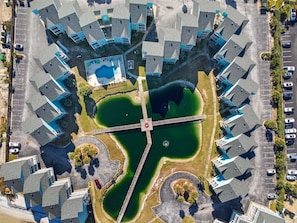 An aerial view of a residential area with a central green space, a bridge, and multiple buildings with blue accents. - Baywatch G5 (Pensacola Beach)