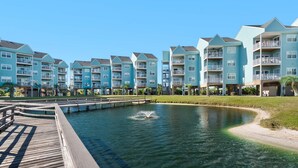 A waterfront residential building with multiple balconies, a wooden dock, and a small water feature. - Baywatch G5 (Pensacola Beach)