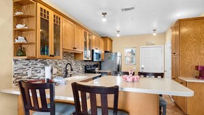 A kitchen with wooden cabinets, a tiled backsplash, a central island with bar stools, and a microwave. - Baywatch G5 (Pensacola Beach)