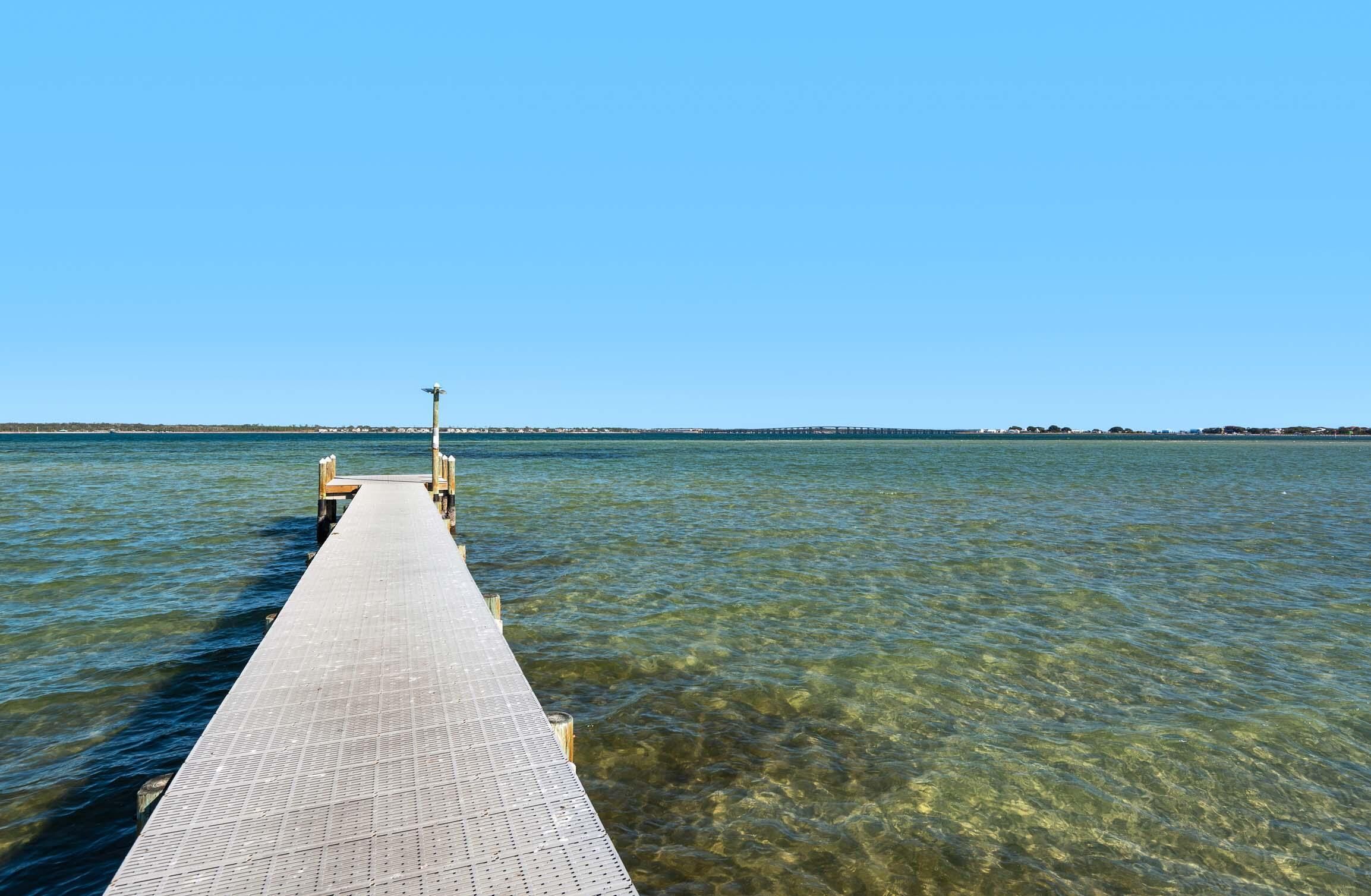 A clear view of a wooden pier extending into a calm body of water, with a clear sky above.