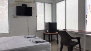 A room with a bed, a TV on a stand, a chair, and a window with frosted glass. - David Houses (Nusa Dua)
