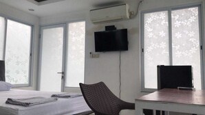 A room with a bed, a chair, a table, a flat-screen TV, and an air conditioning unit. - David Houses (Nusa Dua)