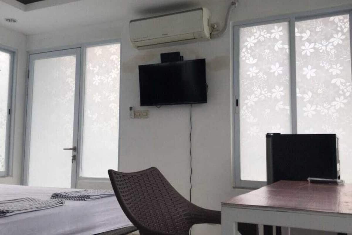 A room with a bed, a chair, a table, a flat-screen TV, and an air conditioning unit.
