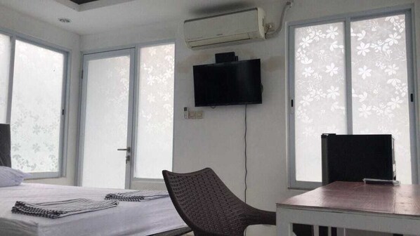 A room with a bed, a chair, a table, a flat-screen TV, and an air conditioning unit. - David Houses (Nusa Dua)
