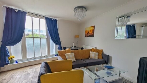 A living room with a sofa, armchair, coffee table, and a large window with curtains. - Stylish & Spacious 1 bed flat next to station (London)