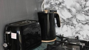 A kitchen with a black toaster, a black coffee maker, and a gas stove. - Stylish & Spacious 1 bed flat next to station (London)