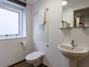 Et badeværelse med toilet, vask, spejl og vindue.