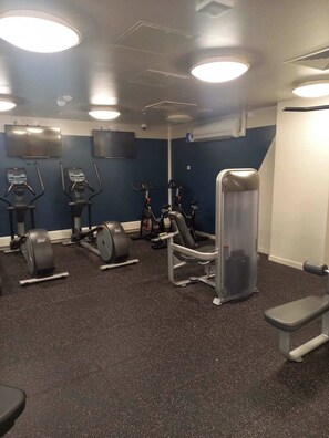 Et fitnessrum med træningsudstyr, herunder løbebånd, motionscykler og en vægtbænk.