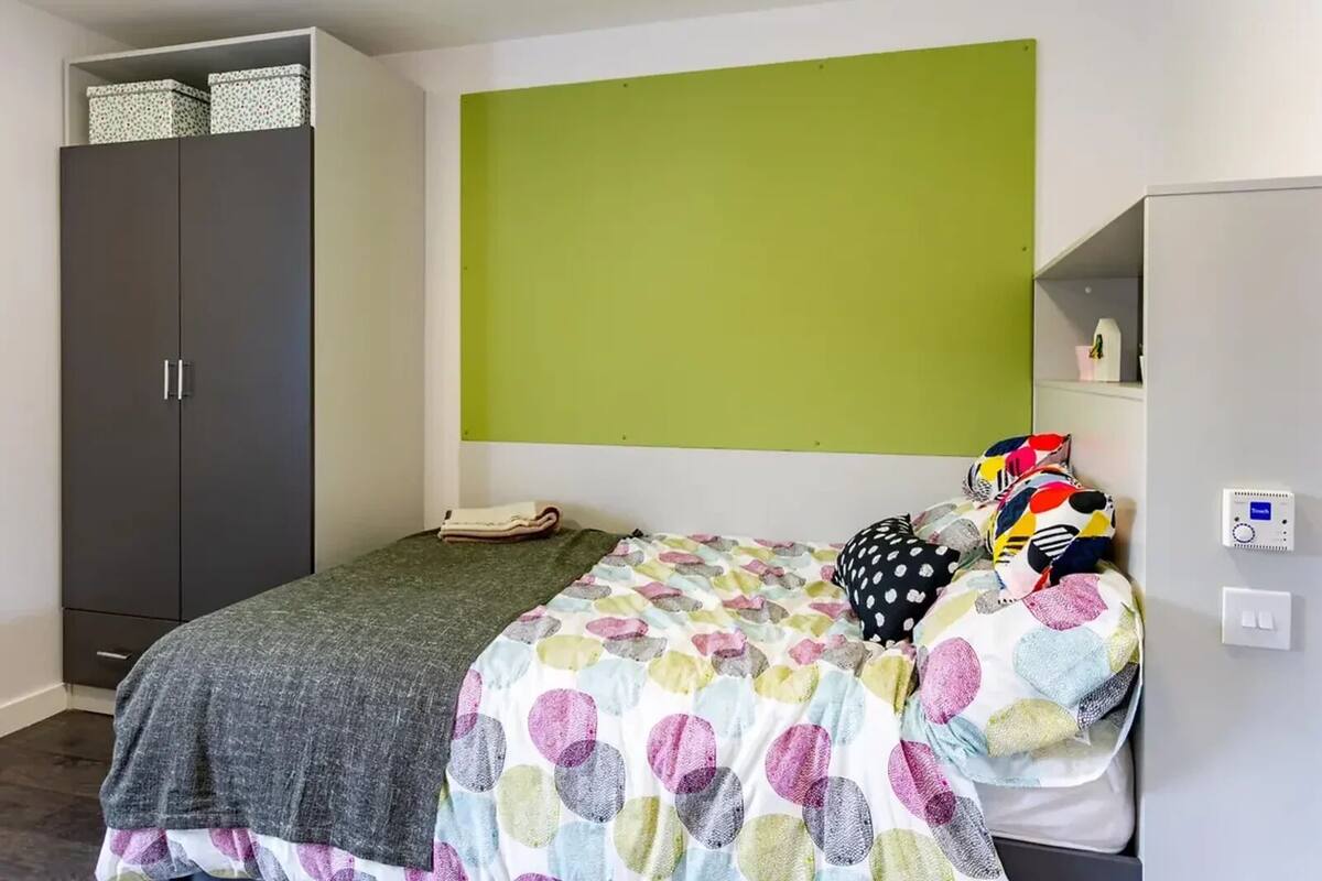 Une chambre à coucher avec un lit, une armoire, un mur vert et une étagère avec divers objets.