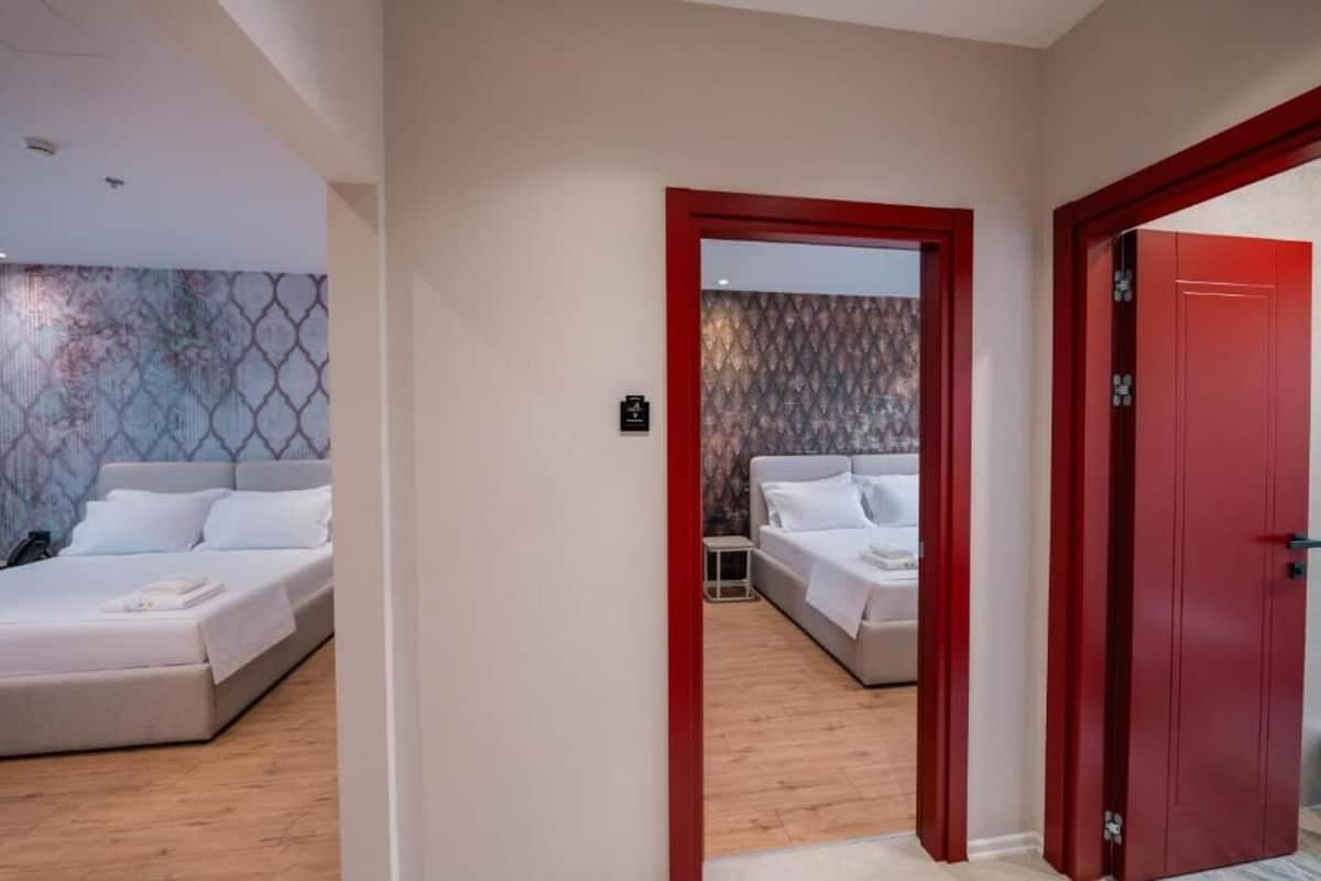 A hotel room with a bed, a bedside table, and a red door.