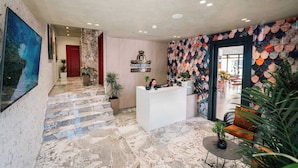 Un hall d’hôtel doté d’un escalier en marbre, d’un comptoir d’accueil et d’un mur décoré d’écailles de poisson.