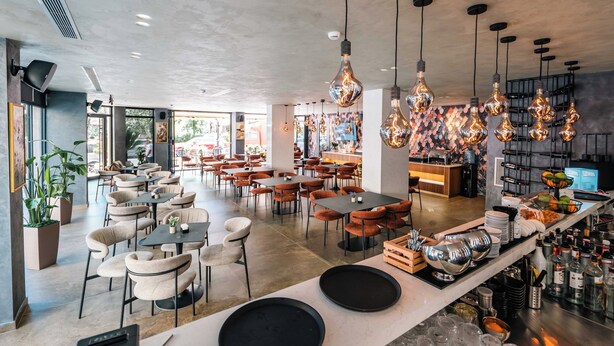 Un café moderne doté de plusieurs espaces de détente, de luminaires suspendus et d’un comptoir de bar proposant une variété de produits.
