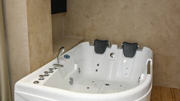 A white bathtub with multiple jets in a corner of a room with beige walls and wooden flooring.