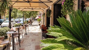 Un espace café en plein air avec des tables et des chaises, un coin salon abrité et des plantes en pot.