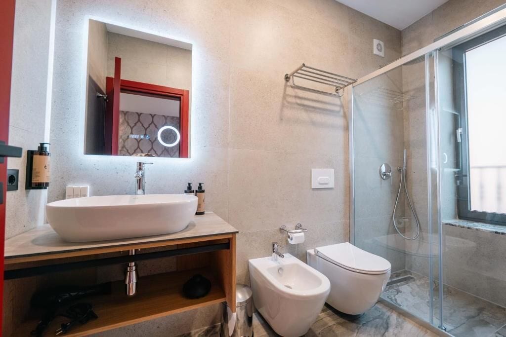 A modern bathroom with a large sink, bidet, toilet, and a glass shower enclosure.