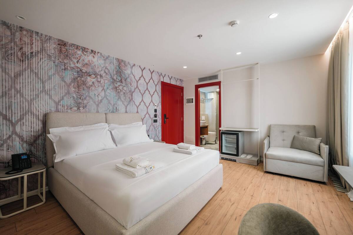 A modern hotel room with a large bed, a TV, a chair, and a desk.