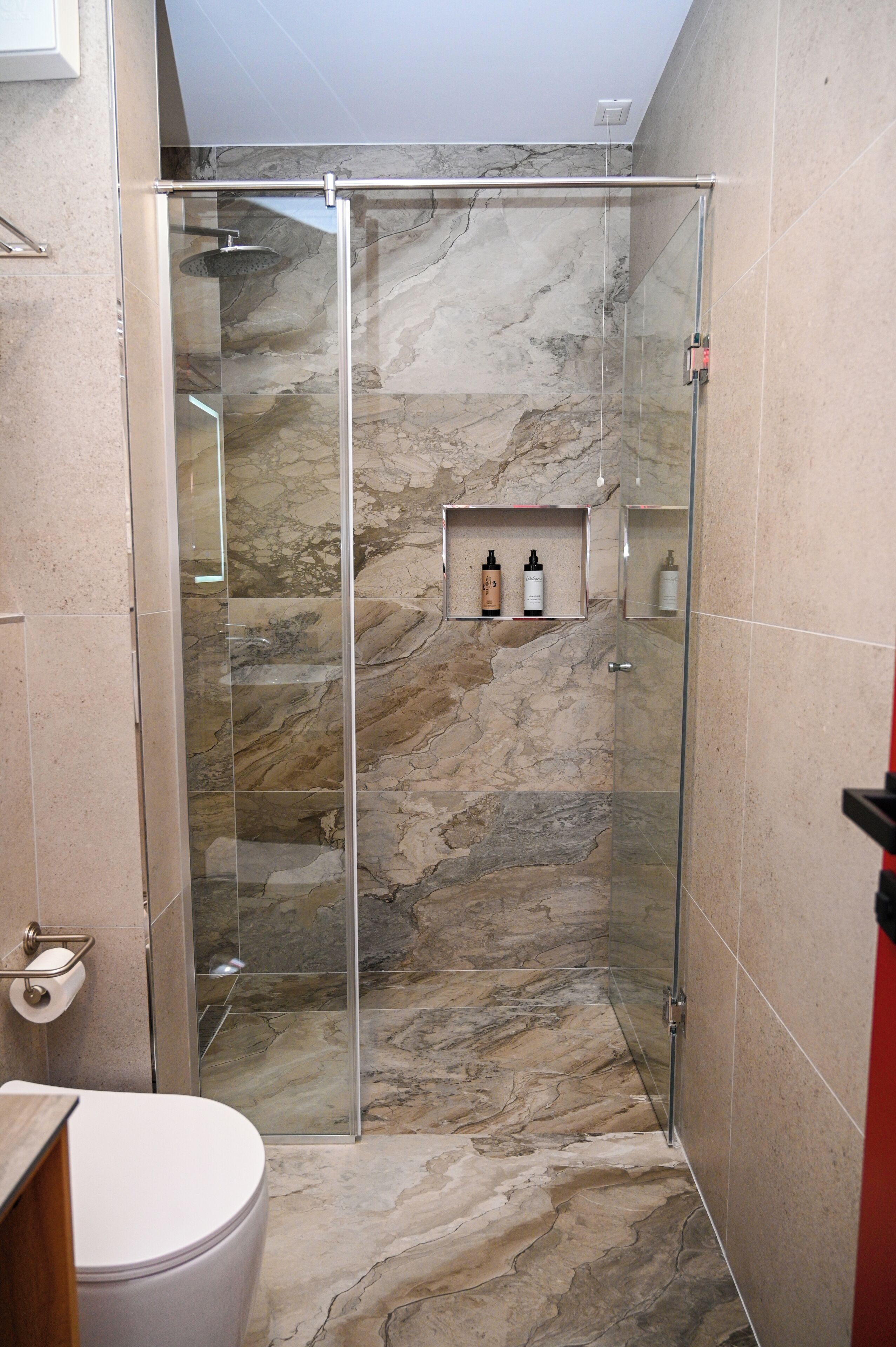 Une salle de bain avec une douche en verre, des murs en marbre et des toilettes.
