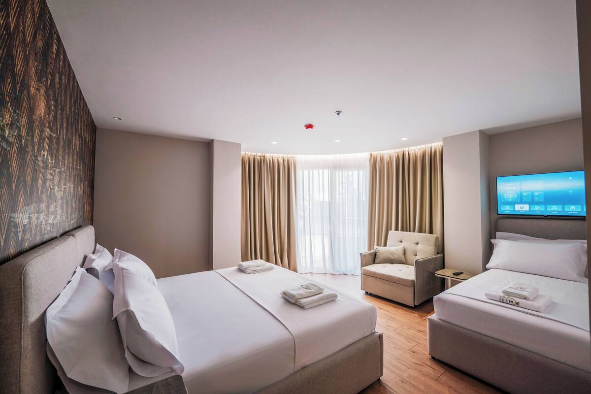 A hotel room with two beds, a TV, a chair, and a desk.