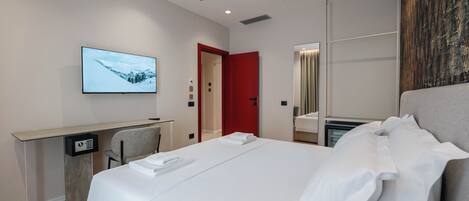 Ein modernes Hotelzimmer mit einem Bett, einem Schreibtisch mit Computer, einem Fernseher und einer roten Tür.
