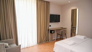 A hotel room with a bed, a desk, a chair, a TV, and a large window with curtains.