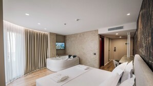 Une chambre d’hôtel moderne dotée d’un grand lit, d’un jacuzzi et d’un téléviseur fixé au mur.