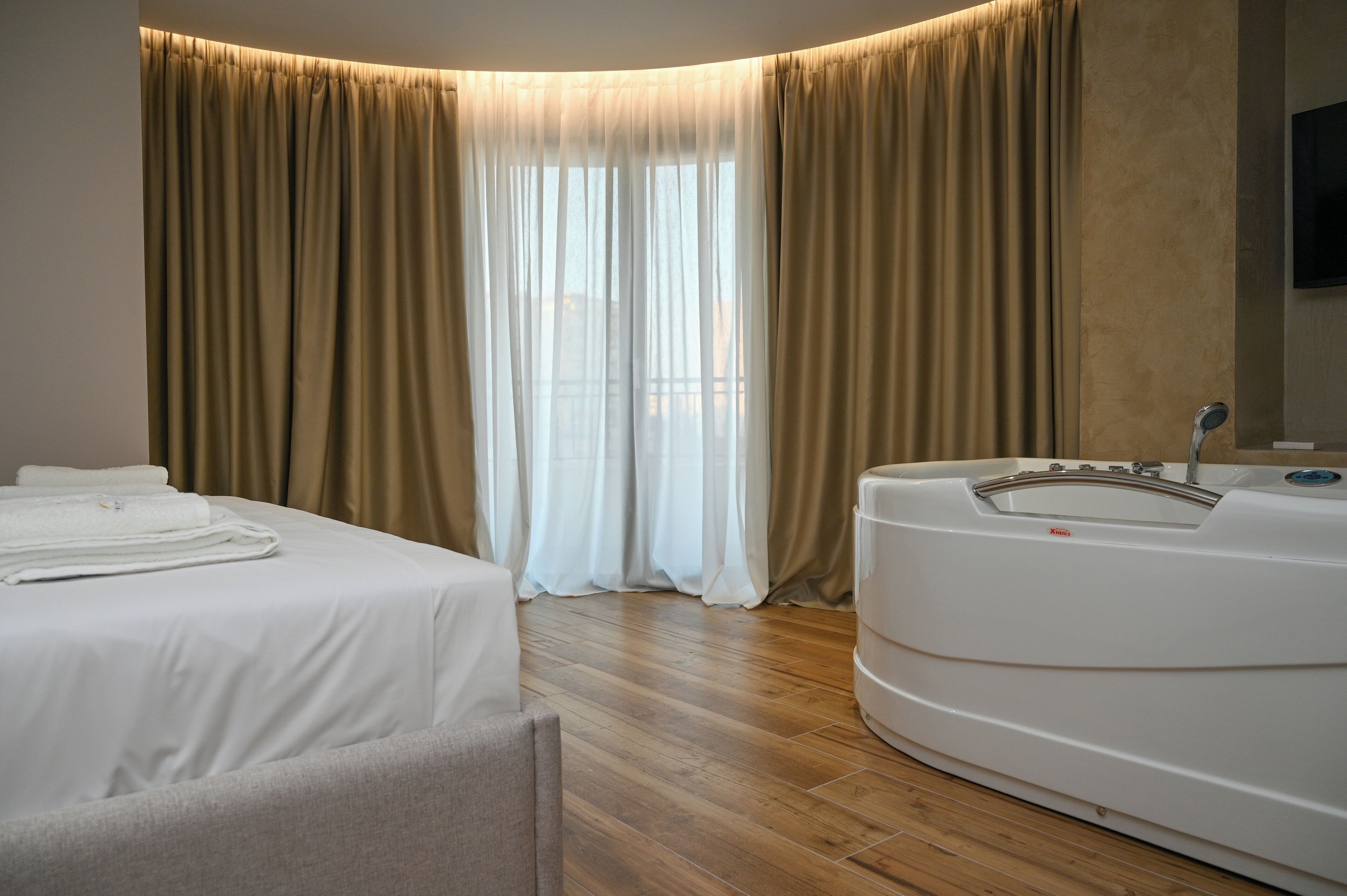 Habitación de hotel con cama, sofá, bañera y un ventanal grande con cortinas.