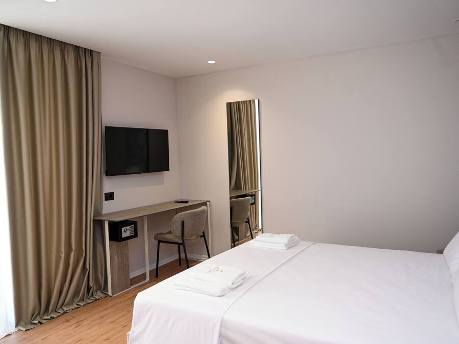 Una camera d'albergo con un letto, una scrivania, una sedia, una TV e uno specchio.