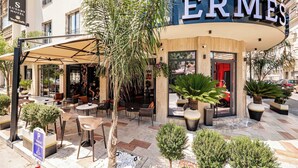 Un espace extérieur aménagé avec des tables et des chaises, un palmier et un panneau indiquant l’hôtel de luxe Hermès.