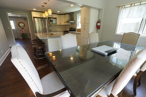 Une cuisine moderne dotée d’appareils électroménagers en acier inoxydable, d’une table à manger en verre et de tabourets de bar.