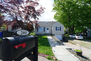 Une boîte aux lettres avec le numéro de maison 205, une pelouse, un trottoir et une voiture garée.
