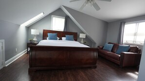 Een slaapkamer met een groot bed, een bruine leren bank, een plafondventilator en een dakraam.