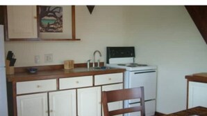 Una cocina compacta con armarios blancos, una estufa y un comedor con mesa y sillas de madera.