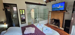 A hotel room with a bed, a glass-enclosed shower, a fireplace, and a television. - chales do parque (Monte Verde)
