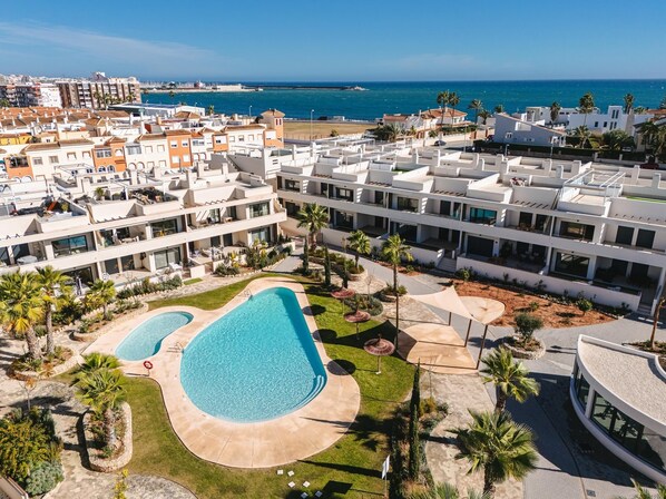 A resort with multiple buildings, a swimming pool, and a view of the sea.
