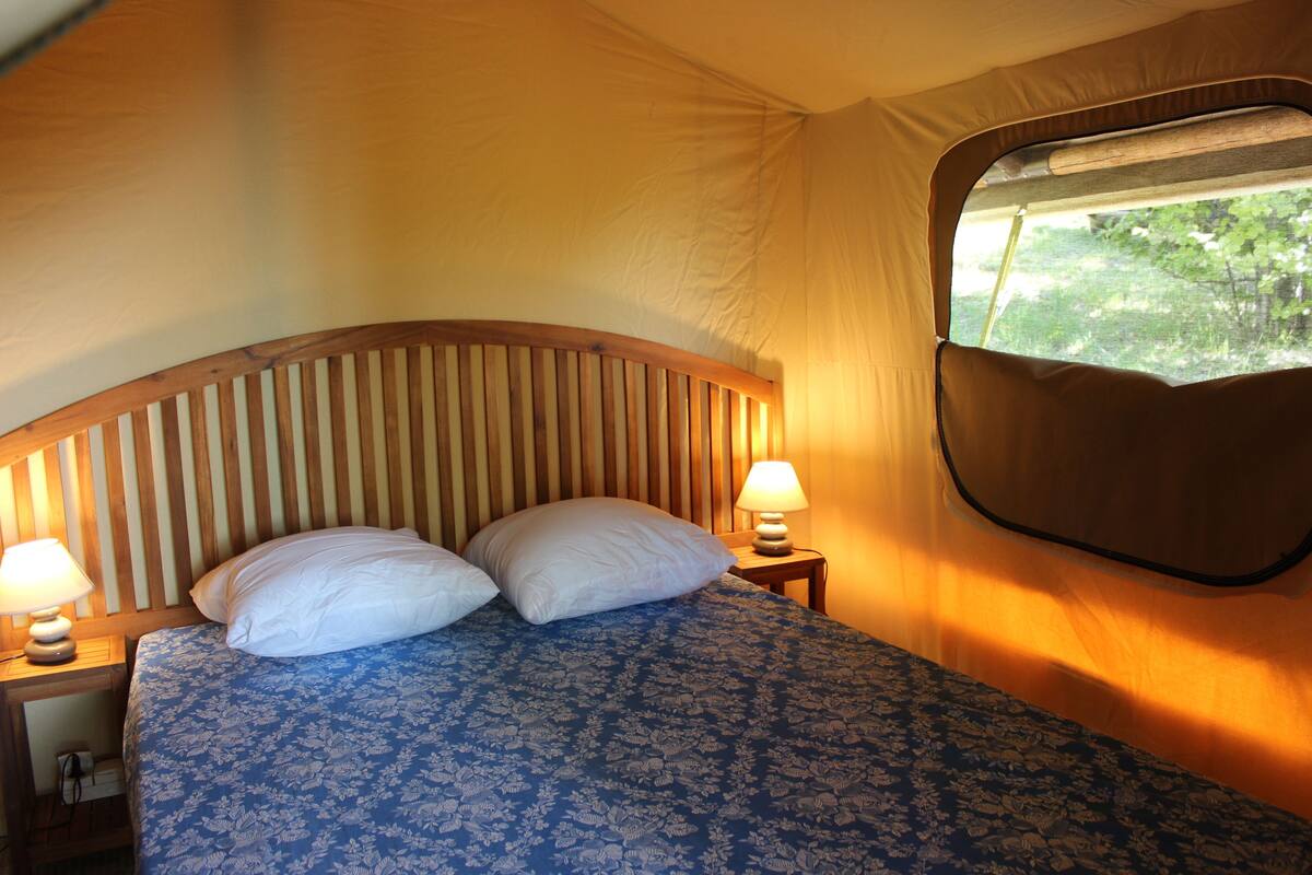 A tent with a bed, two nightstands, and a window.