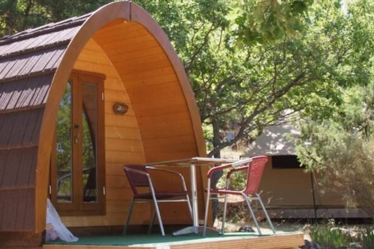 A wooden cabin with a curved roof, a small porch with a table and chairs, and a door leading to the interior.