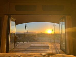 Una puerta abierta que da a una terraza con vista al atardecer sobre un paisaje montañoso.