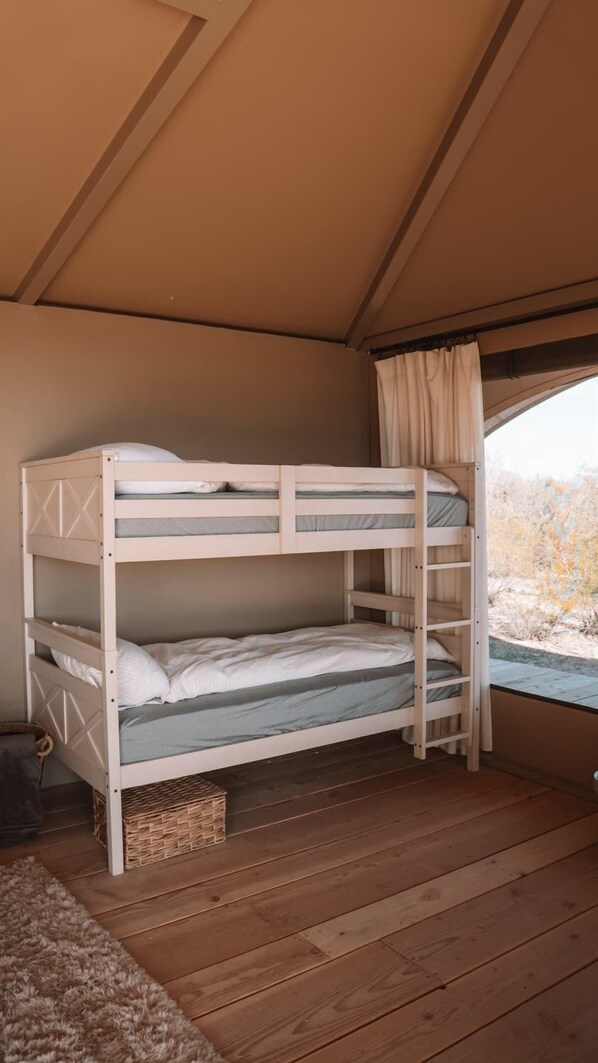 Uma cama de beliche em um quarto tipo tenda, com vista para uma paisagem seca lá fora.
