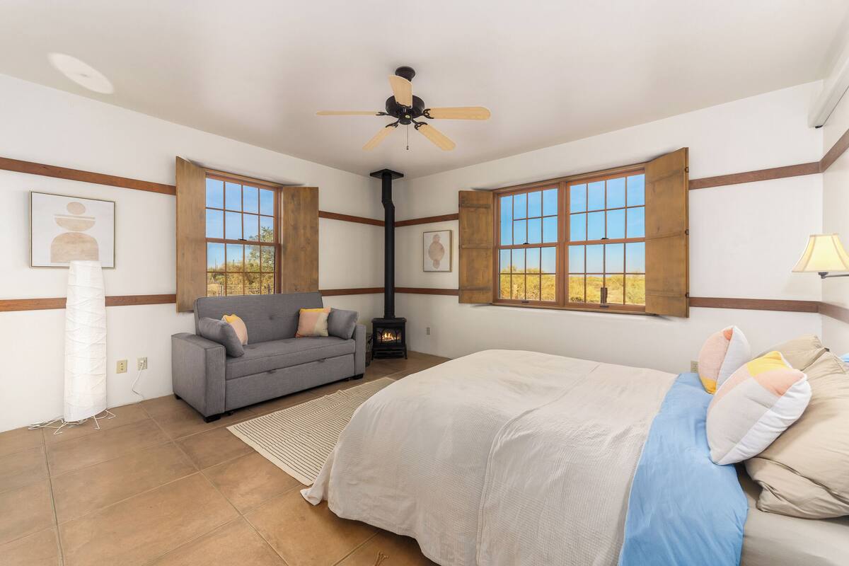 A bedroom with a bed, a sofa, a fireplace, and large windows.