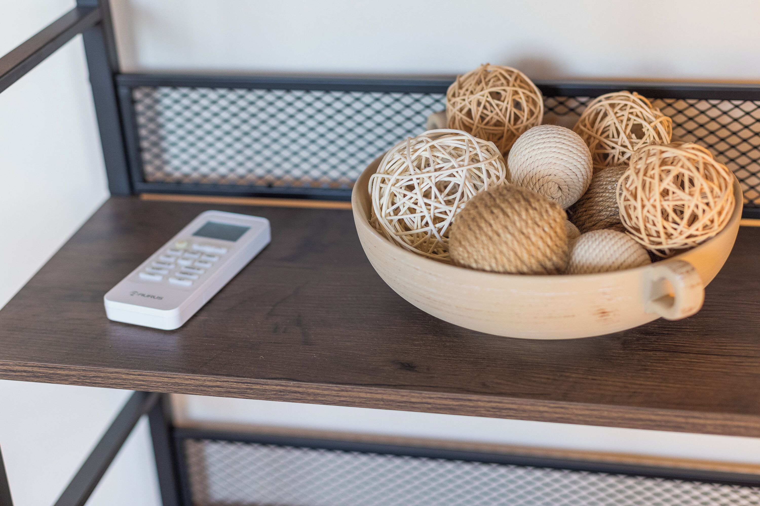 A wooden table with a white remote control and a bowl of decorative balls.
